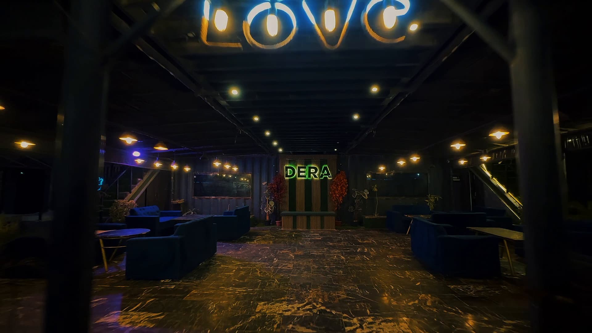 The covered lounge with blue sofas, string lights and a neon LOVE sign