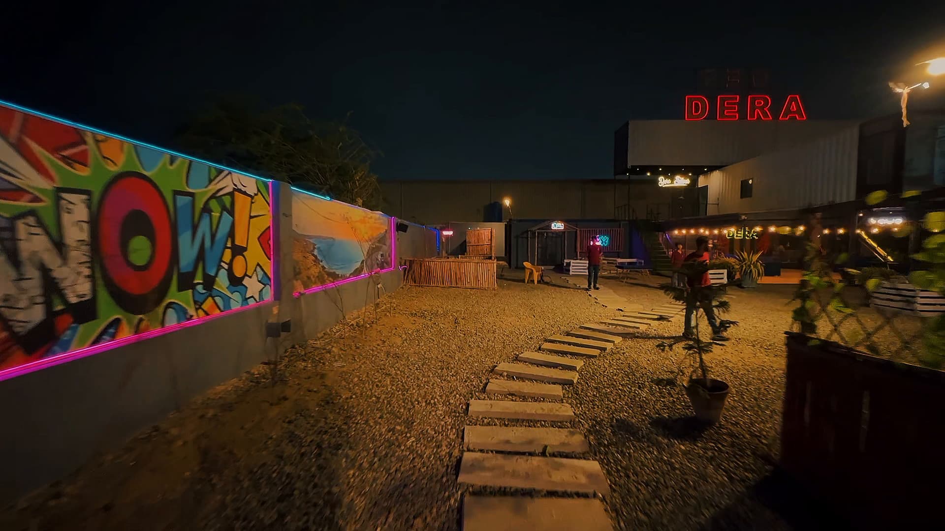 Stone path past a graffiti mural toward the red rooftop DERA sign